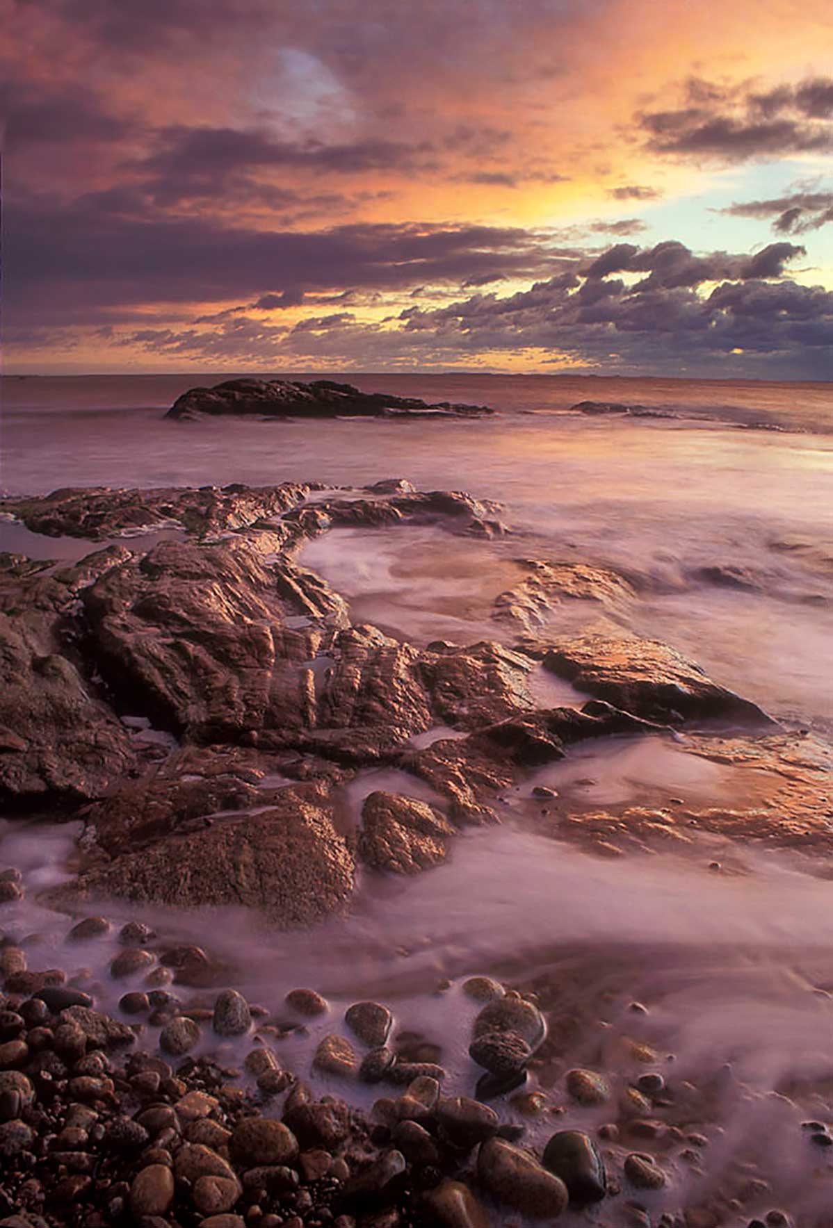 Photograph of water coming on the rocks at sunset on a beach